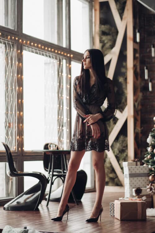 full length of stunning brunette in black dress and heels against christmas tree.