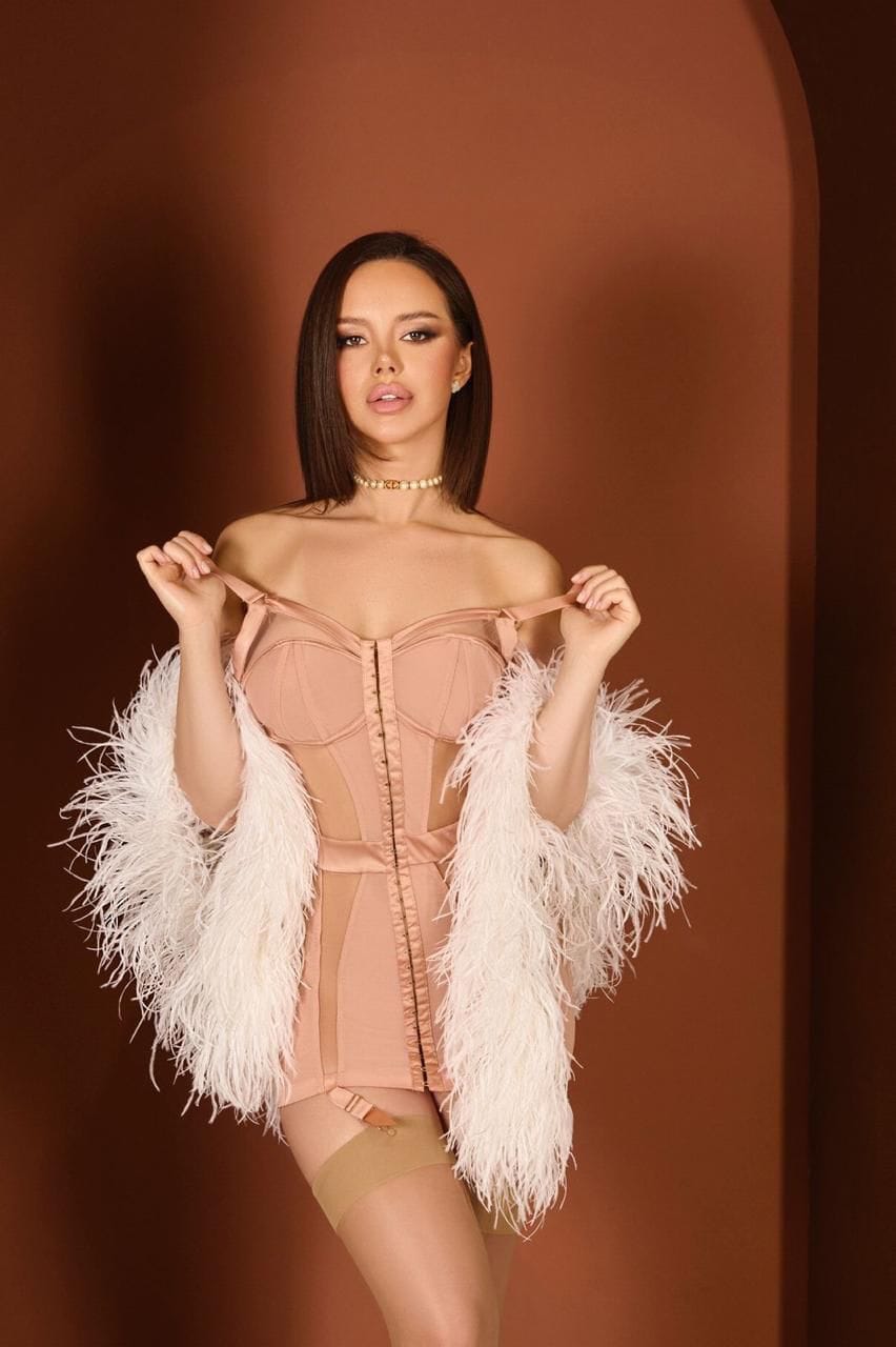 Woman in peach corset dress and white feather shawl.