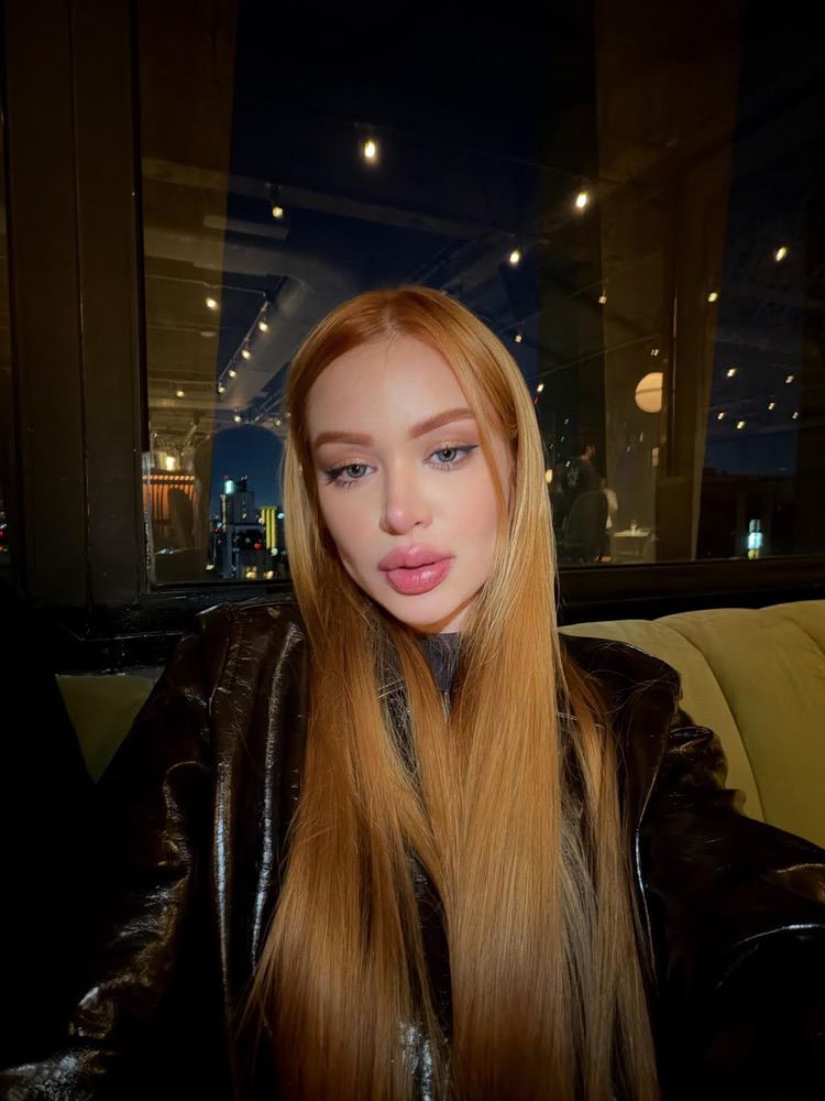 A woman with long strawberry-blonde hair wearing a leather jacket.