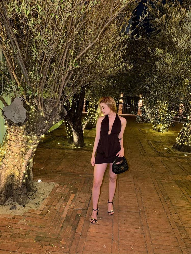 Woman in dark dress standing on fairy-lit tree-lined path.