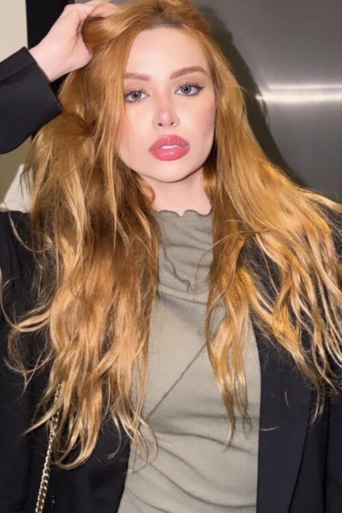 Woman with long strawberry-blonde hair posing in a black blazer.