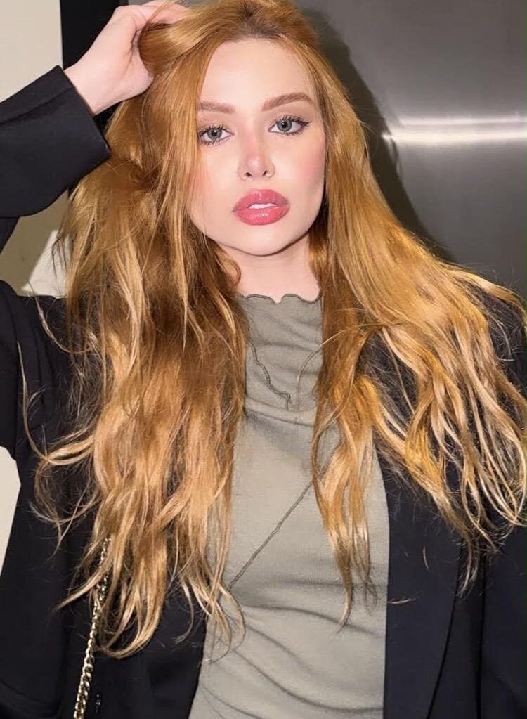 Woman with long strawberry-blonde hair posing in a black blazer.