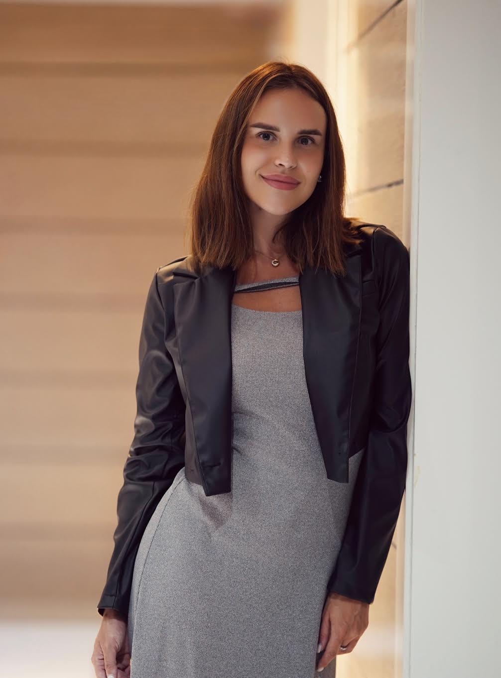 Woman in grey dress and black leather jacket smiling.