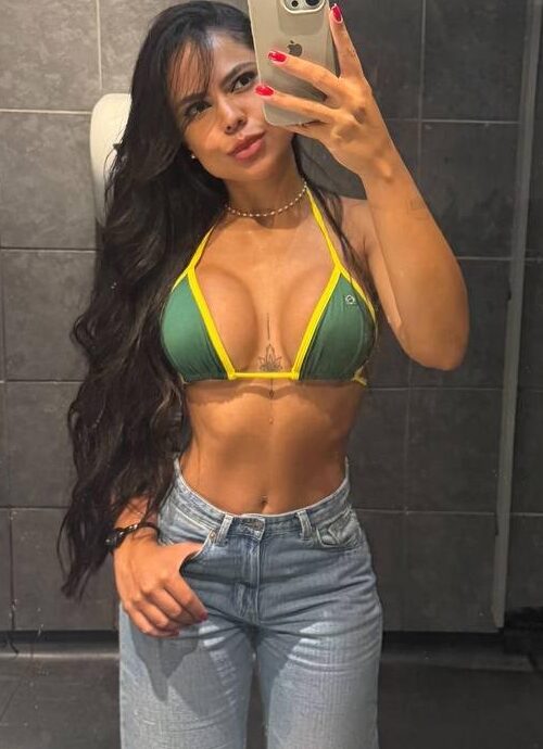 Woman in green bikini and jeans taking a mirror selfie.