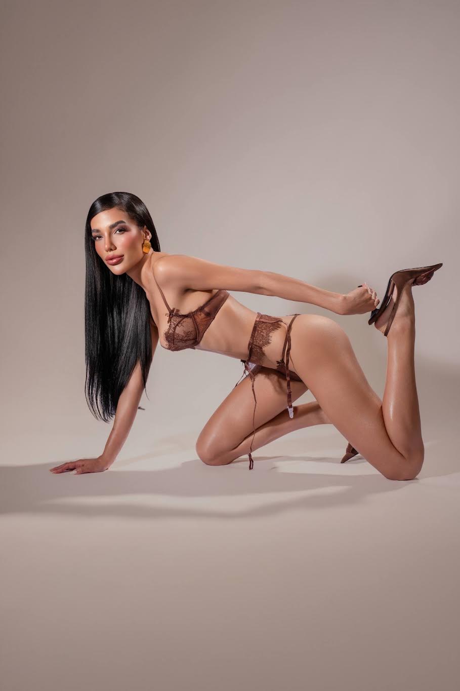 Woman in brown lace lingerie posing on a neutral background.
