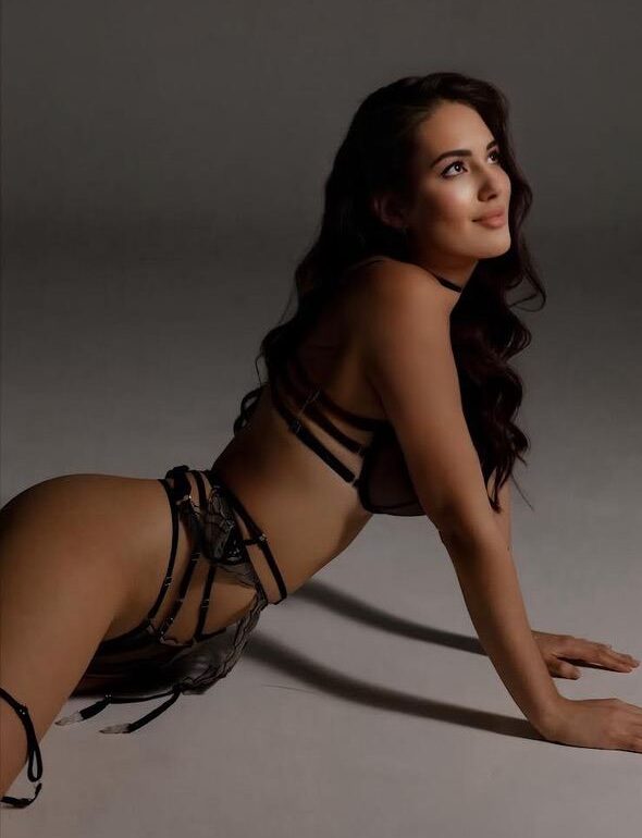 Woman in black strapped lingerie posing on a grey floor.