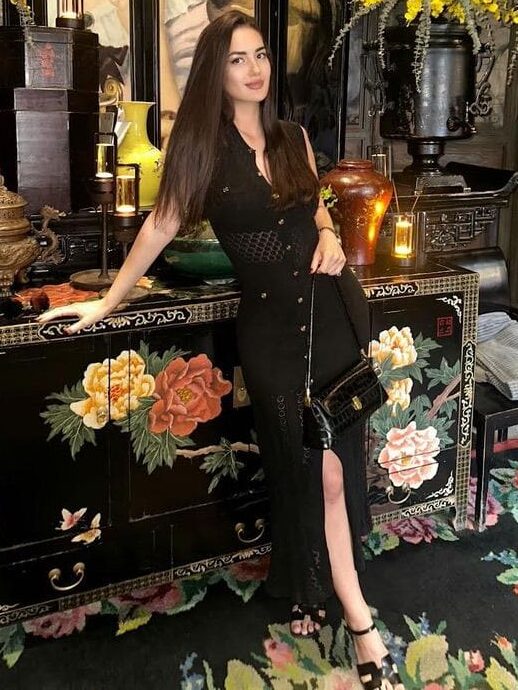 Woman in a black dress posing in an ornate room.