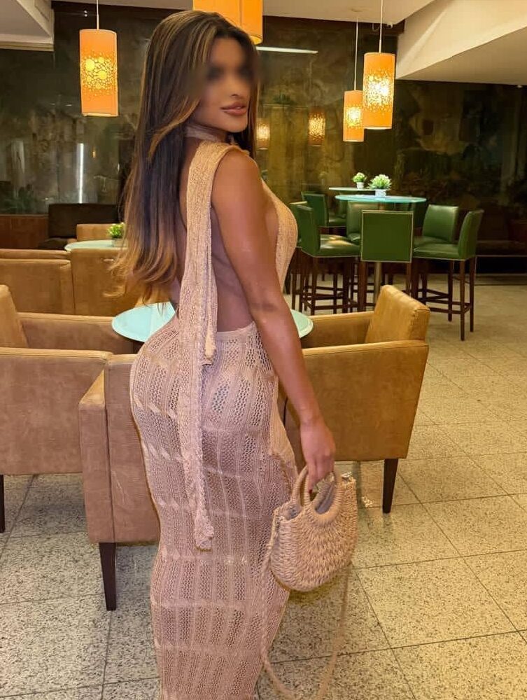 Woman in a tan knitted dress posing in a lounge.