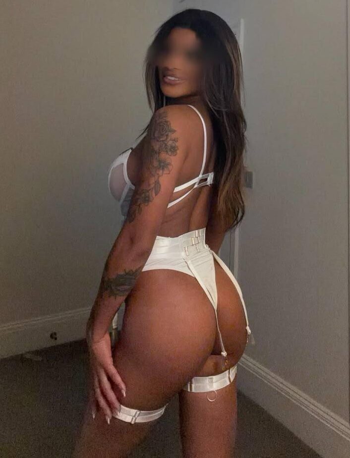 Woman in white lingerie posing with tattoos visible.