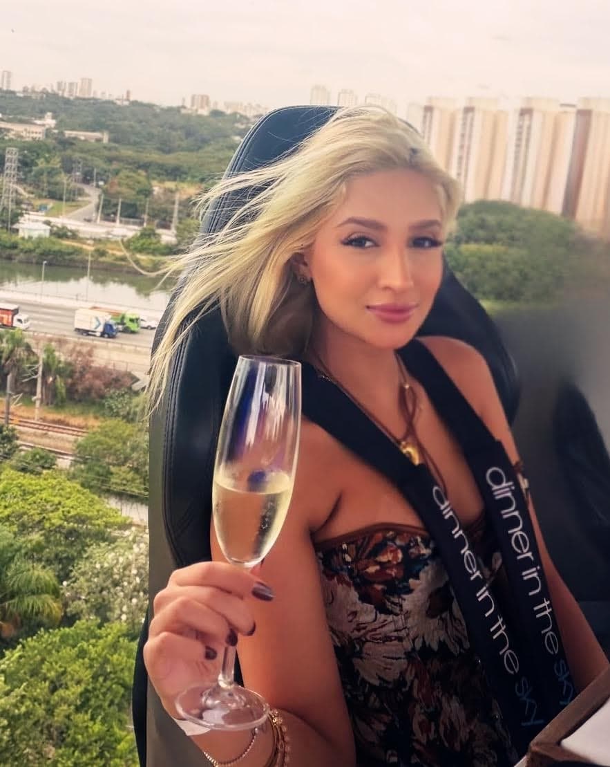 Woman holding a champagne glass at a sky-high dining event.