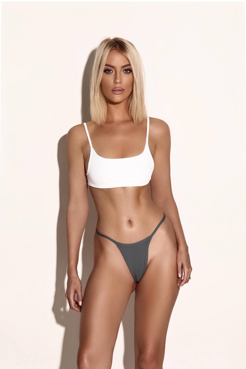 Blonde model posing in white bikini top and grey bottoms.