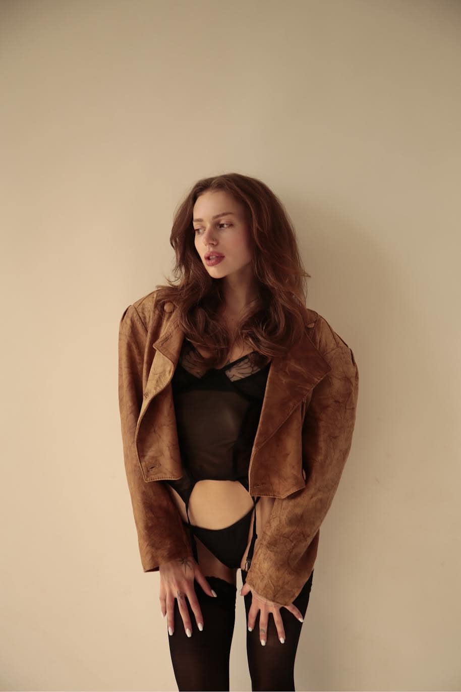 Woman in black lingerie and an oversized brown leather jacket.
