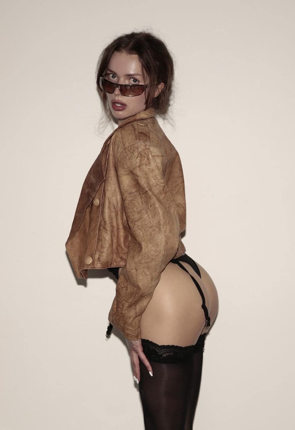 Woman in leather jacket, sunglasses and black stockings posing.