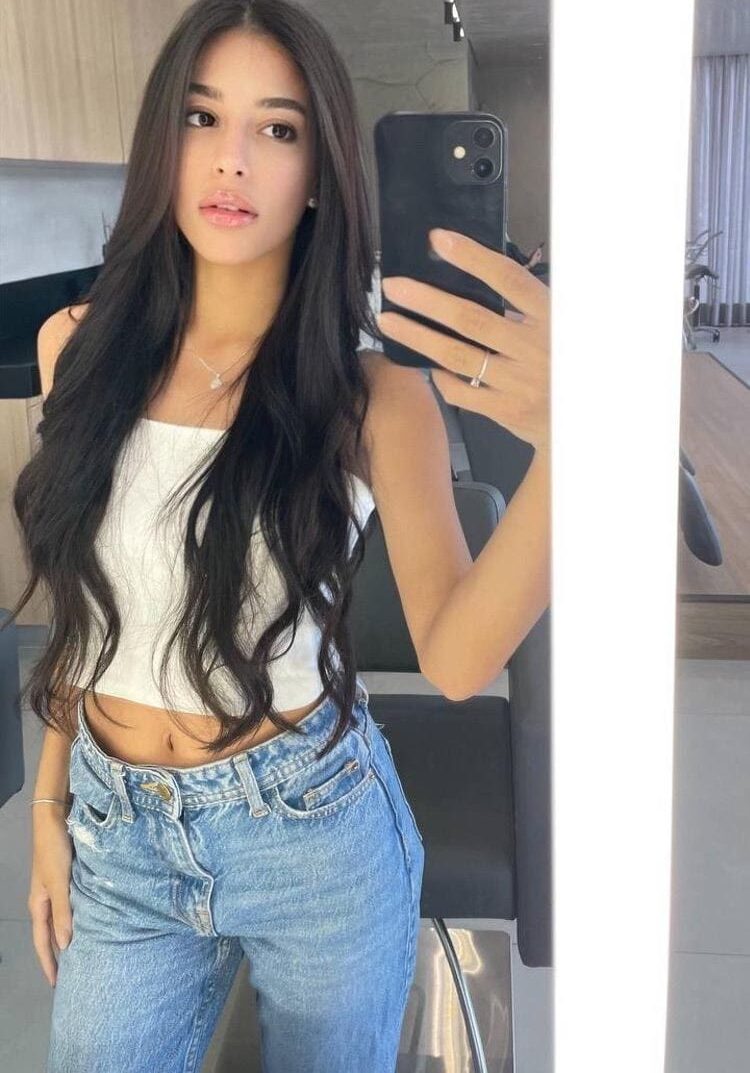 Young woman with long dark hair taking mirror selfie.