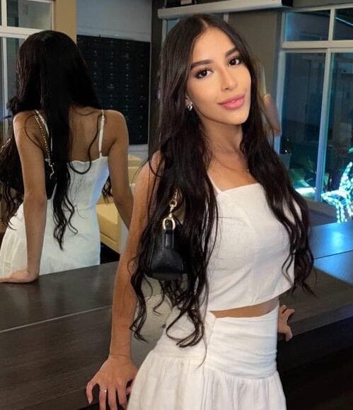 Woman in white two-piece outfit posing near a mirror.