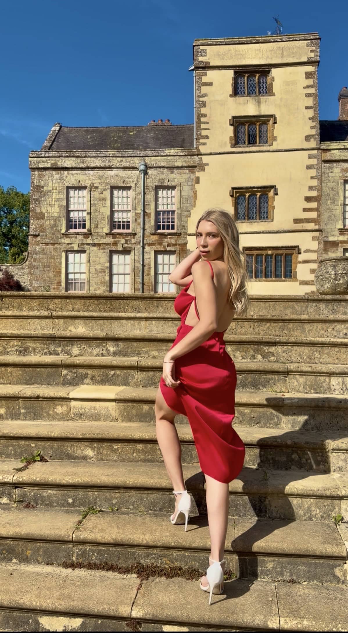 Woman in red dress posing at a grand historic manor.