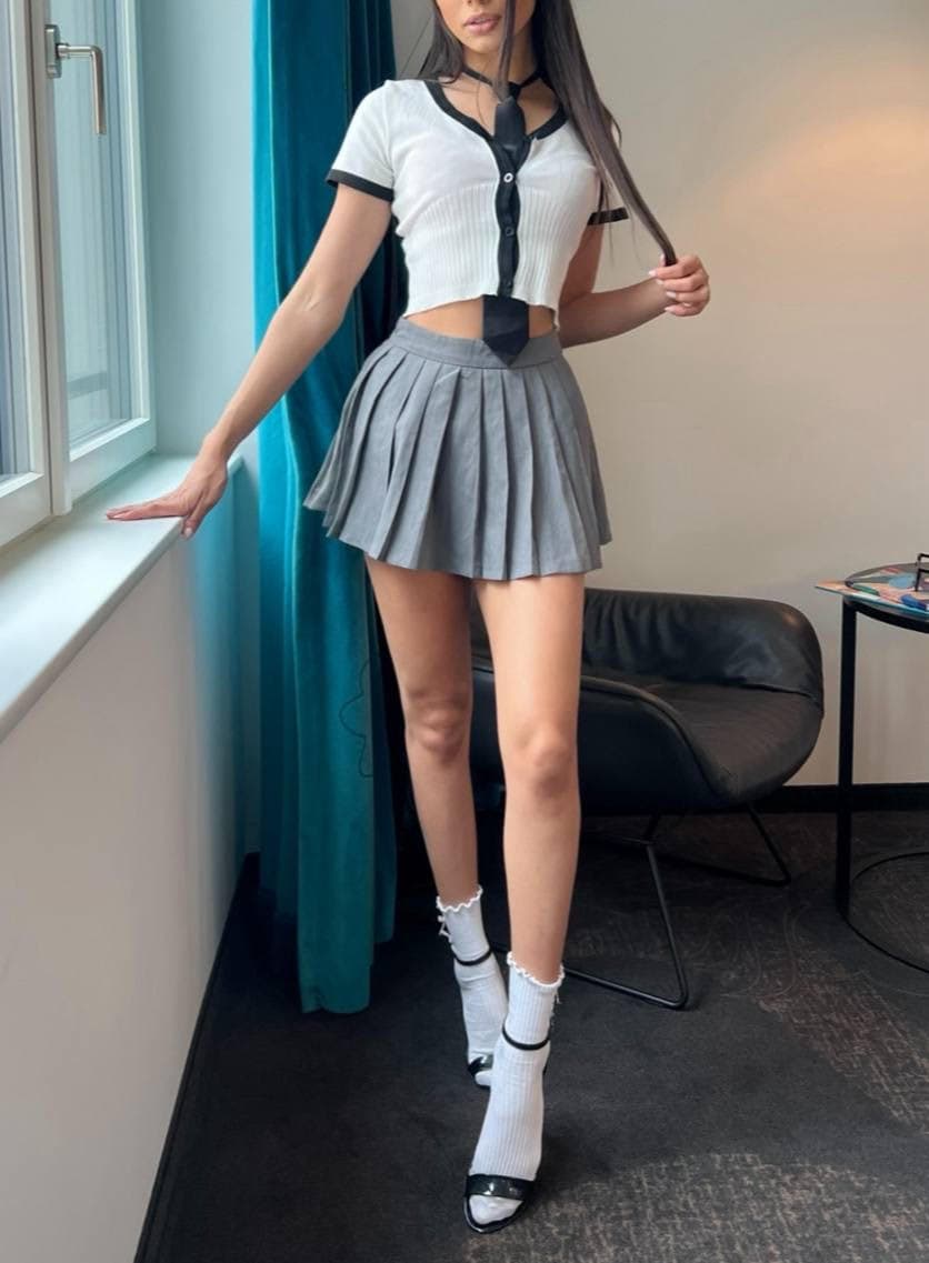 Woman wearing a schoolgirl-style outfit with a grey pleated skirt.