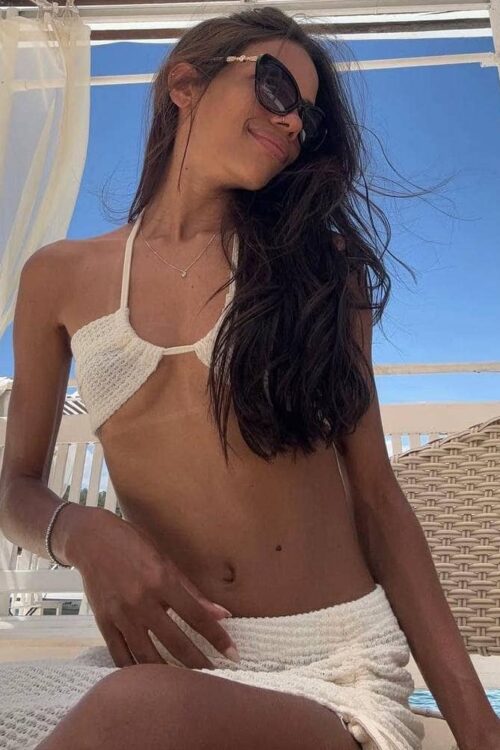 Young woman wearing sunglasses and white swimwear on a deck.