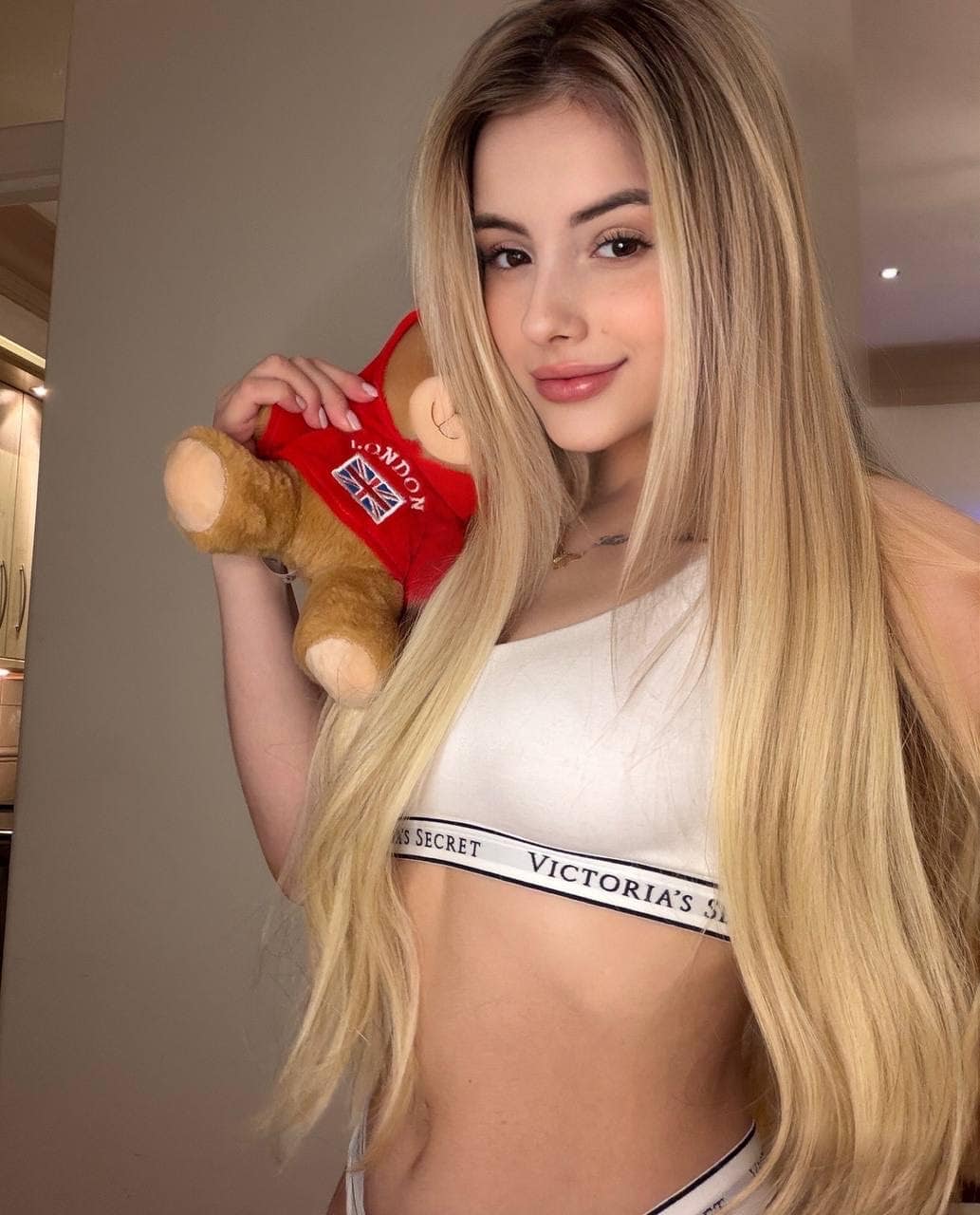 Blonde woman holding a London teddy bear in a white top.