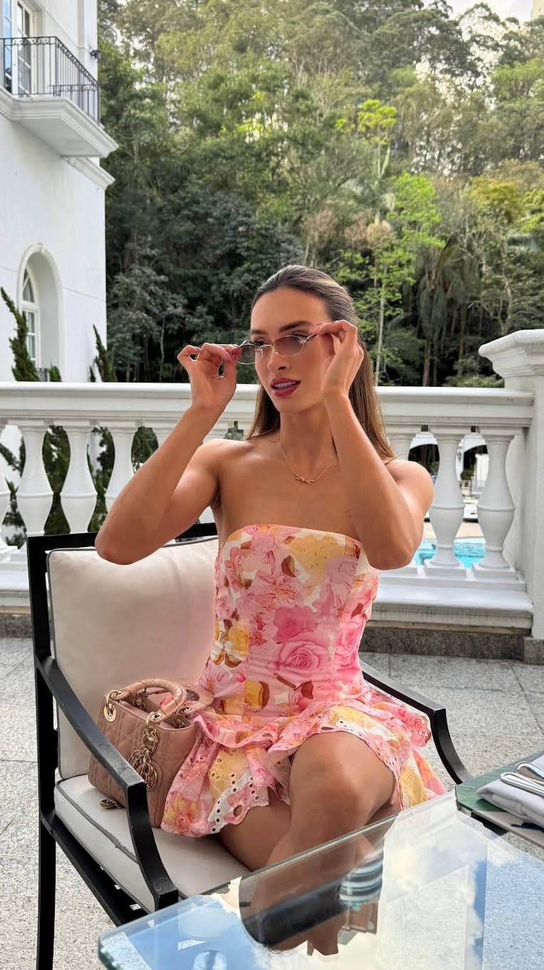 Woman in pink floral dress adjusting sunglasses on a terrace.