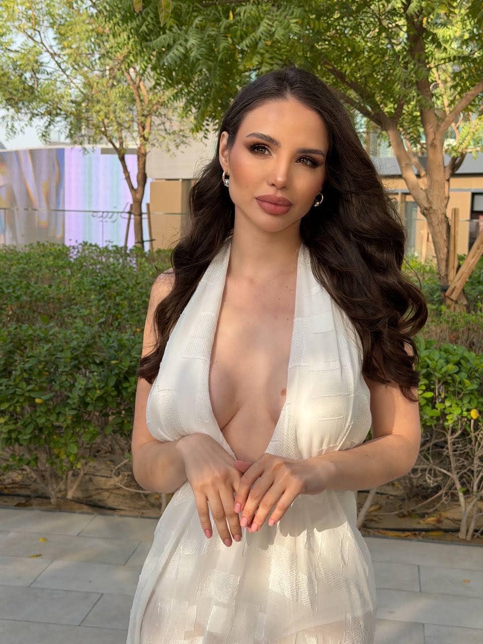 Woman with long dark hair in a white halter-neck dress.