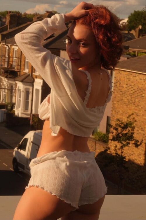 Red-haired woman in white loungewear on a sunny balcony.