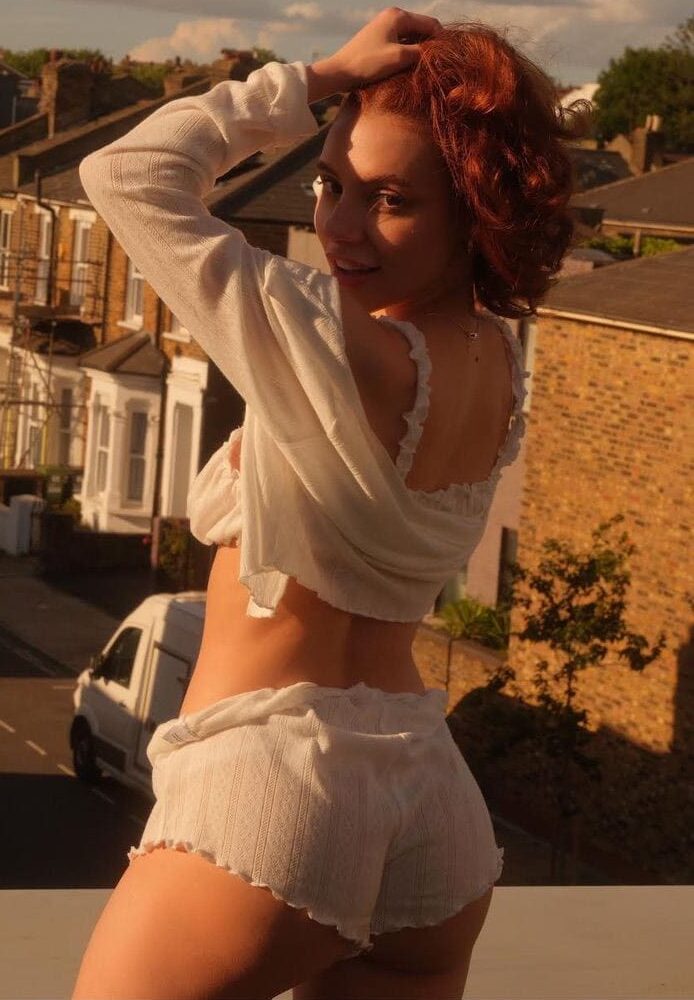 Red-haired woman in white loungewear on a sunny balcony.