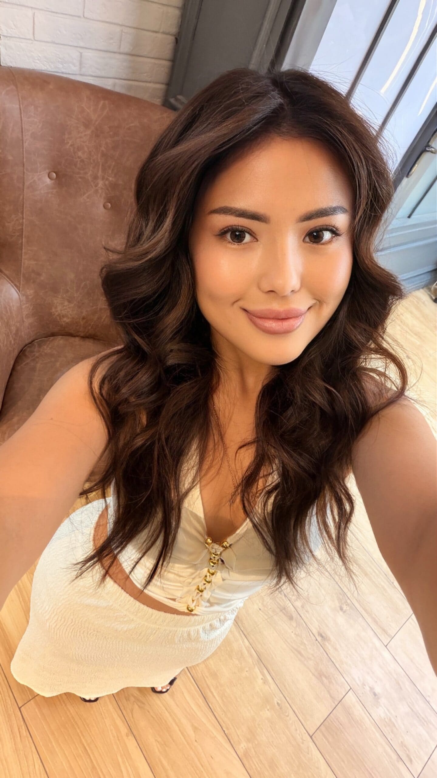 Woman with long wavy brunette hair in a white outfit.