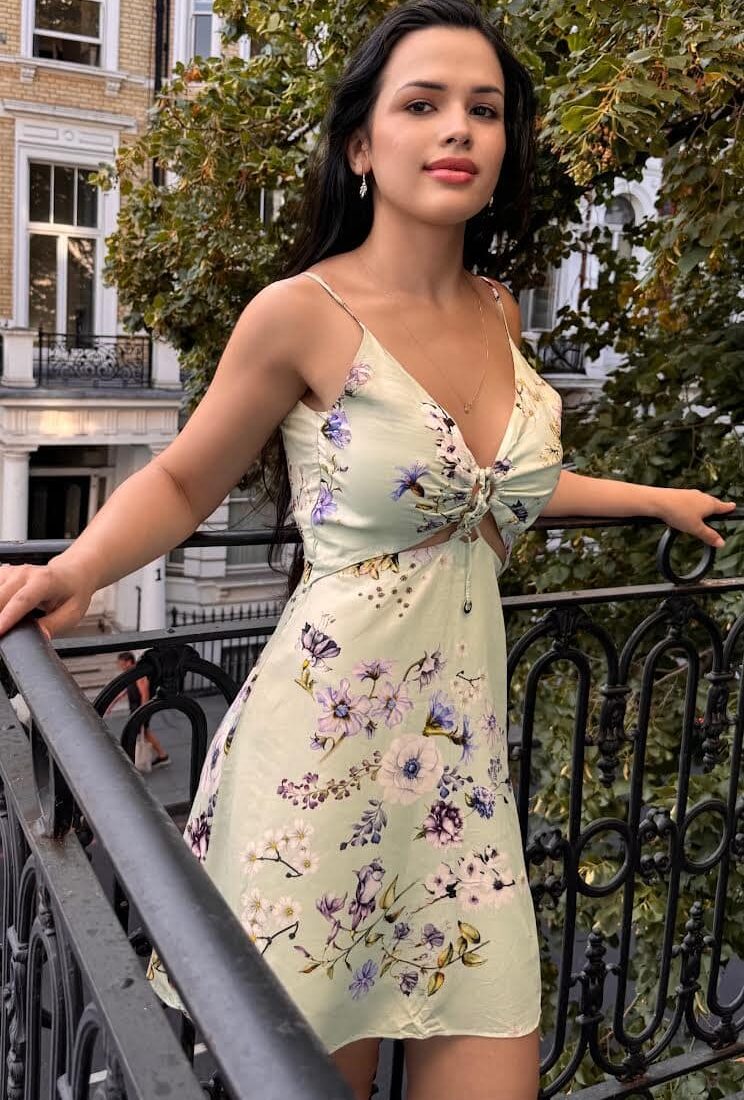 Woman in a floral dress posing on a balcony.