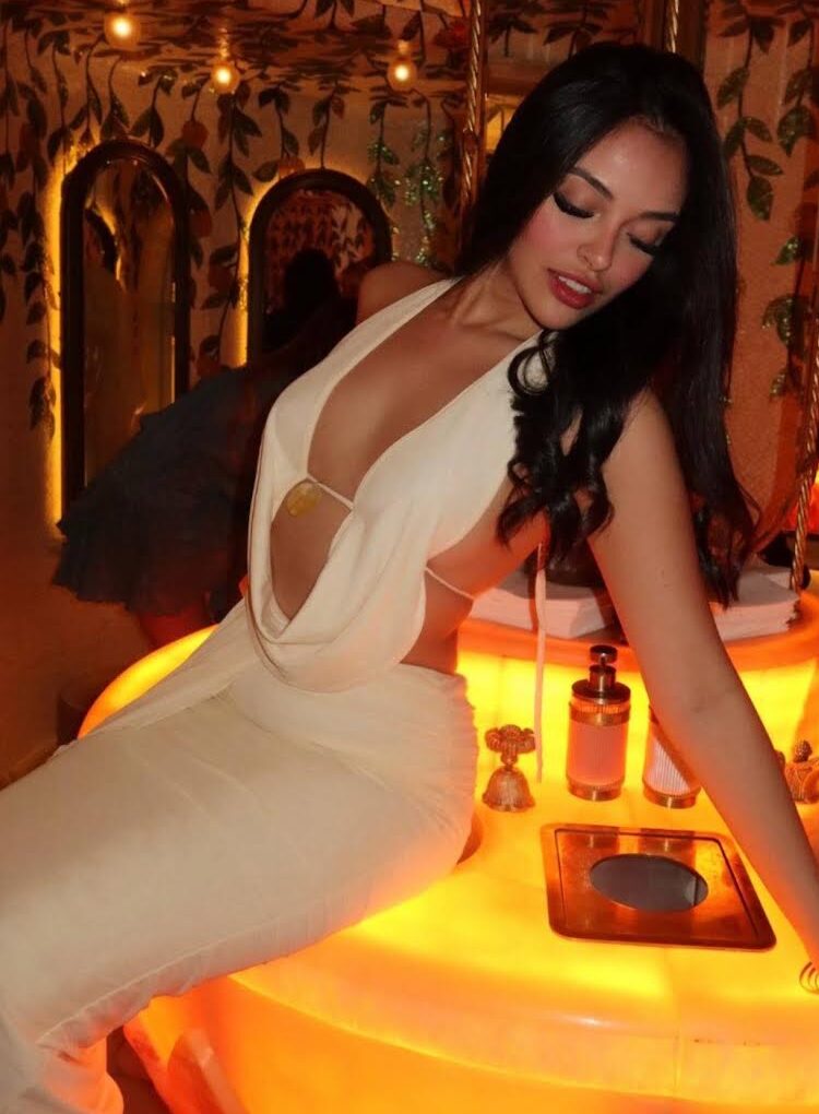 Woman in a white backless dress posing in an ornate room.