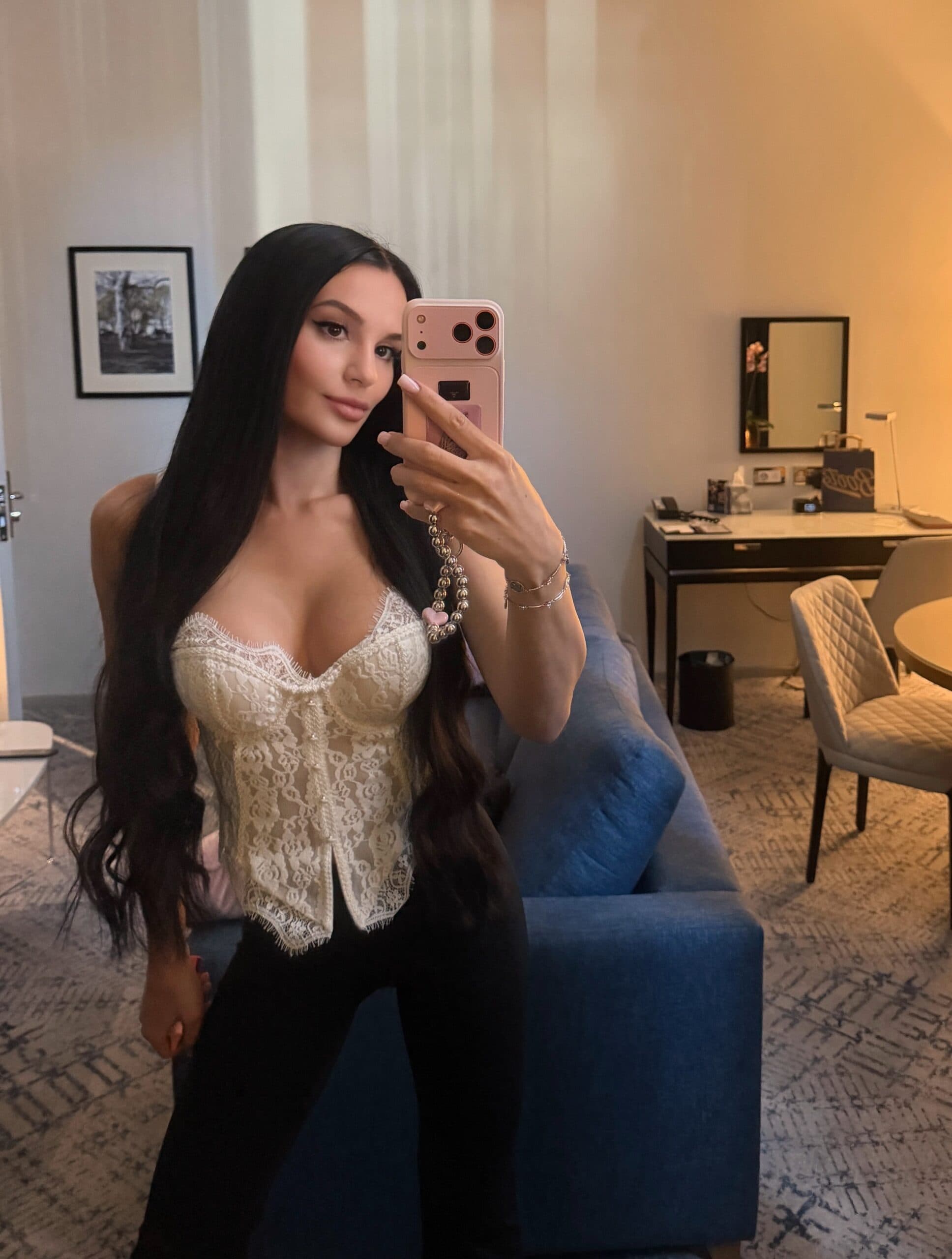 Woman in white lace corset top taking a mirror selfie.