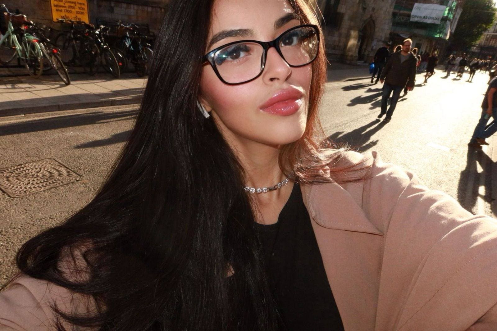 Young woman with glasses and dark hair on a street.