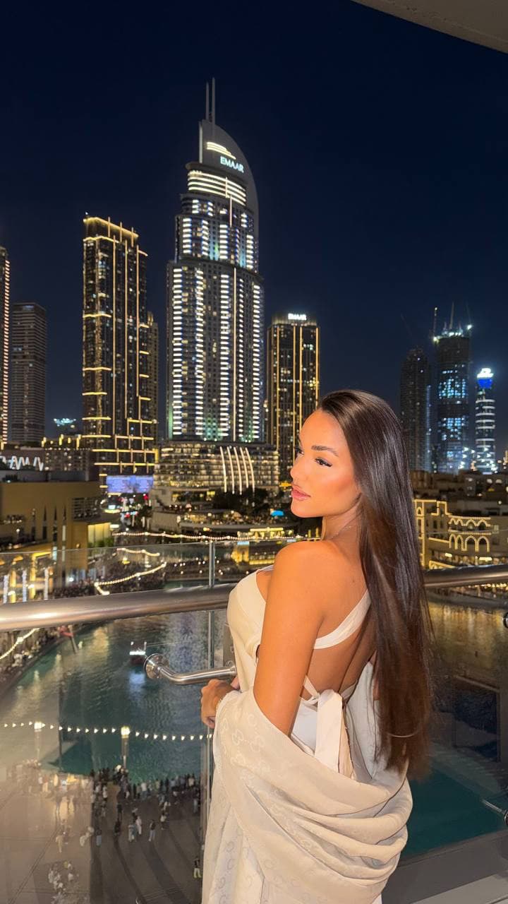 Woman overlooking illuminated Dubai skyscrapers from a balcony at night.